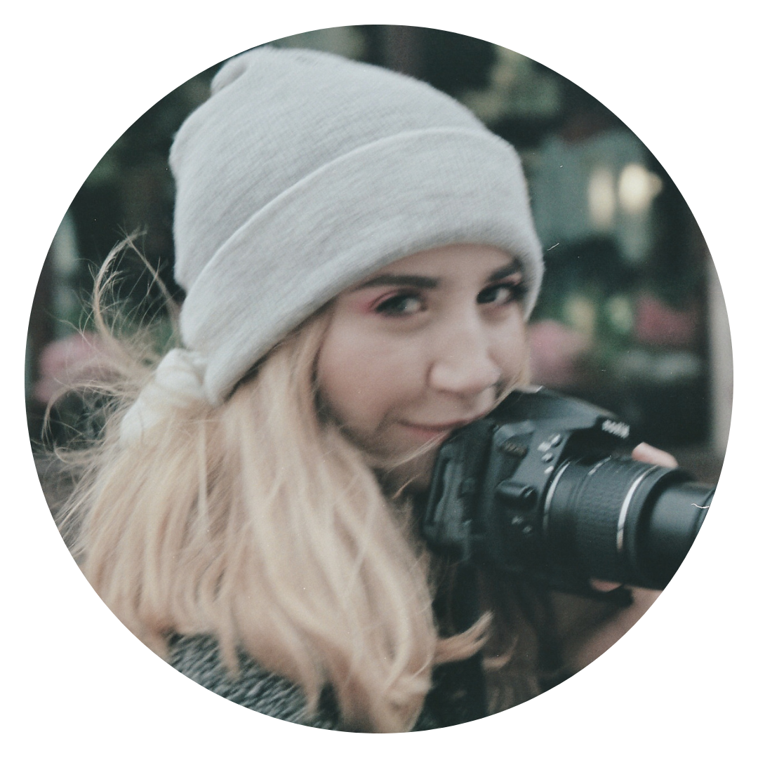 A photograph of the artist, Zoe Green, wearing a grey beanie hat and carrying a camera.